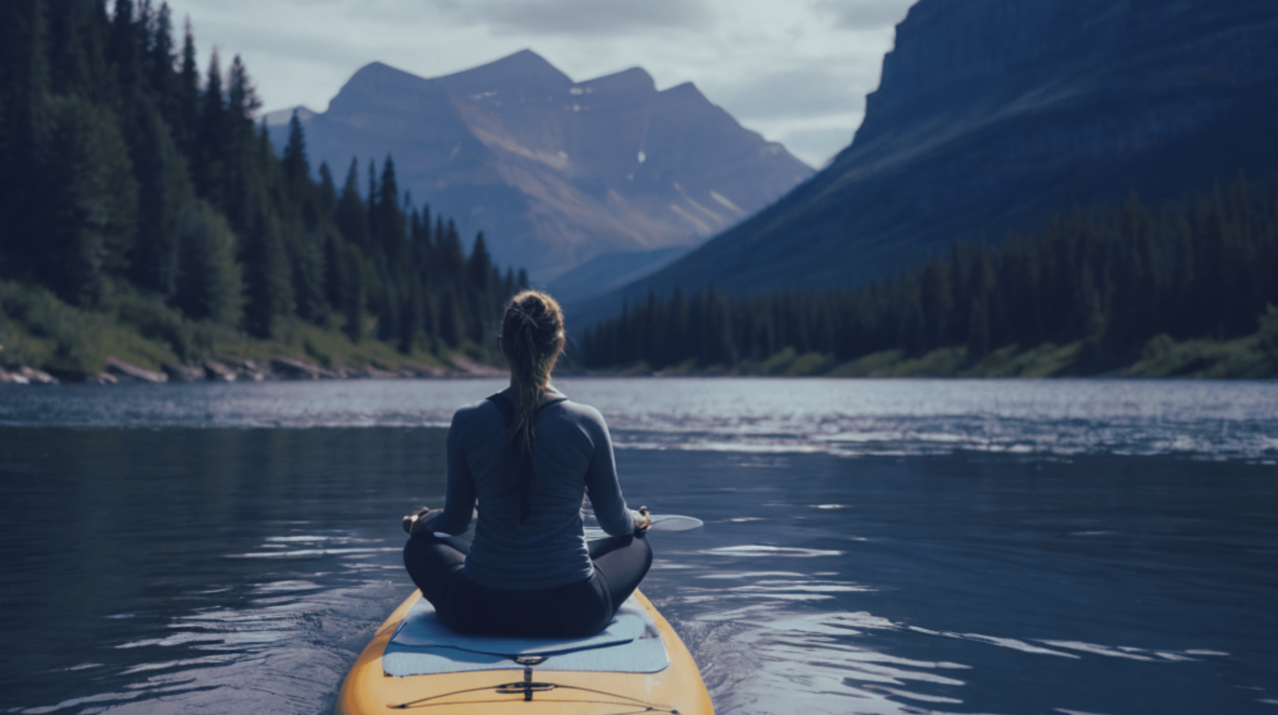 woman seated on paddleboard in yoga pose on a lake near whitefish montana