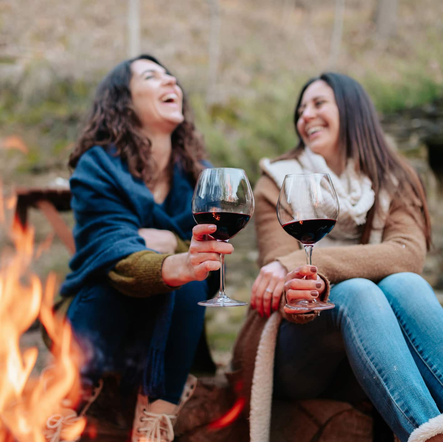 Happy women laughing around a fire and enjoying wine at a Mountainside Collective retreat in northwest Montana